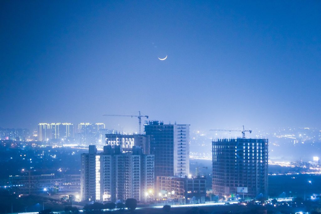 Illuminated cityscape of Greater Noida at night with a crescent moon enhancing the urban skyline.